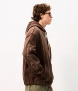 Buzo marrón con capucha y cordones de ajuste, confeccionado en mezcla de algodón y poliéster, con diseño holgado y bolsillo canguro.