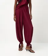 Pantalón de corte aladino con volumen en las piernas, confeccionado en tejido piquet. Presenta cintura elástica y detalle de lazos para anudar en los tobillos.