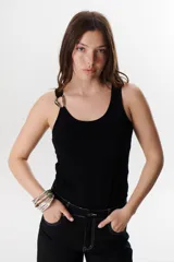 Musculosa negra ajustada al cuerpo con escote redondo y tirantes finos. Presenta un detalle metálico en forma de aro o hebilla en la unión del tirante con el cuerpo de la prenda.