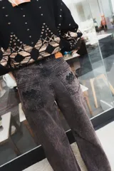 Pantalón de jean de corte recto y tiro medio, con un acabado de teñido ácido en tonos oscuros. Presenta bolsillos traseros con bordados decorativos en color negro y una etiqueta de cuero en la cintura.