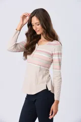 Remera de algodón de manga larga con cuello redondo y botones frontales. Presenta un diseño de rayas horizontales en tonos beige, blanco, rosado y verde menta. Tiene aberturas laterales en el dobladillo y un pequeño detalle metálico dorado en el frente.