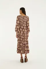 Vestido largo de bordó con estampado ornamental en tonos rosados y dorados, mangas tres cuartos abullonadas con puños elásticos, escote en V con cordones y falda escalonada con vuelo.