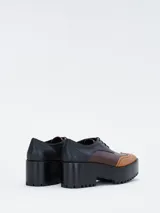 Zapato estilo brogue con plataforma y taco ancho, confeccionado en cuero bicolor con detalles perforados en la puntera y los laterales.