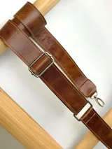 Correa ajustable para cartera confeccionada en cuero marrón con costuras a la vista y herrajes metálicos plateados.