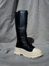 Bota de caña alta color negro con cordones y suela track color crema.