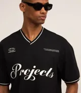 Remera deportiva negra de algodón con cuello en V ribeteado en blanco, mangas cortas con ribete blanco y estampa frontal con la palabra "Projects" en cursiva blanca.