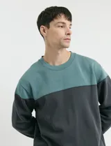 Sweater de tejido circular con diseño color block, combinando una franja superior en color verde y el resto de la prenda en gris oscuro. Presenta cuello redondo y puños en tejido canalé.