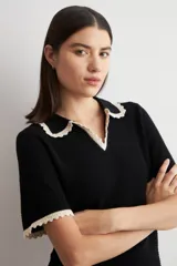 Sweater de punto negro de manga corta con cuello polo y ribetes contrastantes en color beige con detalles de encaje en el cuello y los puños.