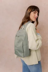 Mochila compacta de color beige, con compartimento principal con cierre, bolsillos laterales y bolsillo frontal con cierre oculto. Cuenta con correas regulables y acolchonadas y asa superior.