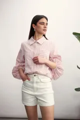 Camisa a rayas verticales color rosa y blanco, con cuello clásico, mangas largas abullonadas y dos bolsillos frontales.