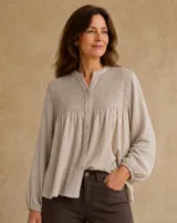 Camisa de lino color beige, con cuello mao, cierre frontal abotonado y detalles de nido de abeja en el canesú y los hombros. Cuenta con mangas largas abullonadas y puños elásticos.