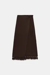 Falda midi pareo de color marrón, con diseño cruzado, cierre lateral con botón interior y lazada. Presenta detalles de bordados y flecos en el bajo.