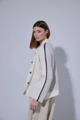 Saco de punto acanalado en color gris claro, con cierre frontal de botones oscuros. Presenta un diseño de bloques de color en las mangas, combinando negro y marrón, y un cuello redondo.