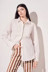Camisa blanca oversize de algodón, con cuello clásico, cierre frontal con botones de nácar y bolsillo en el pecho.