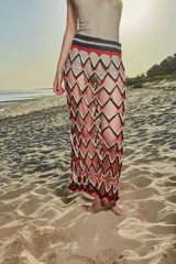 Falda larga tejida a crochet con diseño de red y patrón de rombos en colores negro, rojo y blanco. Presenta una cintura elástica tejida en color negro.