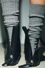 Botín plano de piel color negro, con diseño minimalista, costura central decorativa y cierre lateral mediante cremallera.