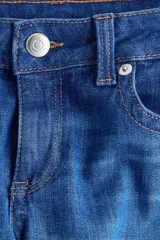 Pantalón jean de denim azul elastizado, de tiro bajo y corte ajustado con botamanga acampanada. Presenta diseño clásico de cinco bolsillos y cierre frontal con botón y cremallera.