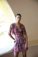 Vestido corto con estampado floral en tonos rojo/fucsia y gris/azul, escote en V, mangas cortas con vuelo y frunces en el delantero y espalda. Posee bolsillos delanteros.