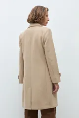 Tapado clásico de corte recto en color beige, con solapas, cierre frontal de botones y bolsillos laterales. Presenta un diseño minimalista y elegante.