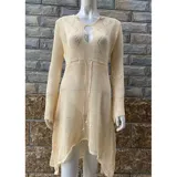 Vestido de playa corto en tejido calado color crema, con mangas largas acampanadas y diseño asimétrico con volado en el ruedo. Presenta un escote redondo con abertura frontal y cordón ajustable.