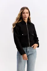 Campera corta de paño color negro, con cierre frontal metálico, cuello camisero y bolsillos frontales con solapa y botón metálico.