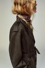 Abrigo largo color marrón oscuro con efecto ante, cuello solapa, manga larga con trabillas en los hombros y bolsillos delanteros de vivo. Presenta un bajo con abertura en la espalda y cierre frontal cruzado con botones, complementado con un cinturón a tono.