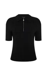 Remera de punto acanalado color negro, con silueta ajustada, cuello polo estructurado, mangas cortas y cierre frontal con cremallera metálica y colgante decorativo.