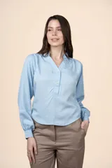 Blusa celeste de tencel con cuello mao, escote en V con botones frontales y mangas largas con puños ajustados.