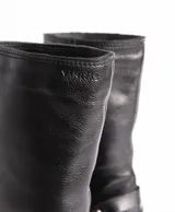 Bota de cuero negra con caña media, punta cuadrada, taco bloque y arnés con hebillas y tachas plateadas.