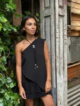 Collar largo tipo lazo con cuentas negras cilíndricas, detalle de pieza metálica central con incrustaciones y terminaciones con dijes metálicos circulares texturizados.