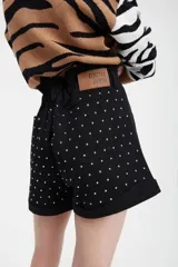 Short negro con pequeños apliques metálicos plateados, tiro alto, pretina con cinturón negro con tachas y cierre frontal con tres botones.