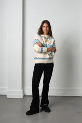 Buzo de tejido de punto con diseño nórdico, cuello redondo acanalado y mangas largas. Presenta un patrón geométrico en tonos celeste, negro y crema.