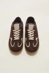 Zapatilla urbana de gamuza color marrón con detalles en beige, cordones claros y suela de goma tipo caramelo.