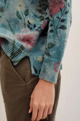 Sweater de punto con estampado floral en tonos rosados sobre base verde, cuello redondo y mangas largas.