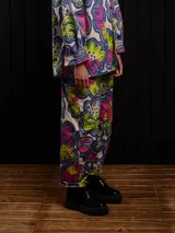 Pantalón de gabardina con estampado floral multicolor, corte carrot fit, tiro medio, estilo carpintero, con botón de metal personalizado, pieza carpintera y parche trasero personalizado.