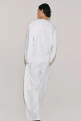 Camiseta blanca de manga larga y corte regular fit, confeccionada en mezcla de algodón y lino. Presenta cuello panadero con cierre frontal de botones y bajo recto.
