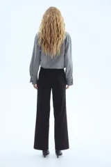 Pantalón negro de vestir, tiro alto, con piernas anchas y corte recto. Presenta pliegues marcados en el frente y cierre frontal oculto.