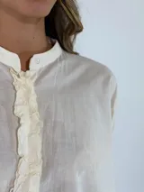 Camisa de corte oversize y diseño holgado, con cuello camisero, cierre frontal de botones y mangas largas con puños abotonados. Presenta un ruedo redondeado y una caída fluida.