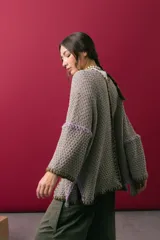 Saco oversize de tejido de punto en color beige, con mangas caídas y detalles de bordado a mano en tonos verde y lila en los bordes y costuras.