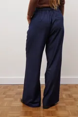 Pantalon de corte recto y pierna ancha, confeccionado en tejido tipo denim oscuro. Presenta tiro alto, cintura con cierre frontal y bolsillos laterales funcionales.