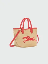 Bolso tipo tote pequeño de paja trenzada color natural, con ribetes y asas de cuero rojo. Presenta un logo bordado de dos caballos galopando en color rojo en el centro.