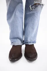 Bota corta estilo western confeccionada en cuero descarne color marrón, con taco cuadrado de madera y punta ligeramente afinada.