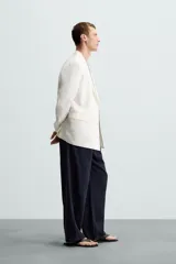 Blazer color crudo de lino y algodón, corte regular, con cuello de solapa de pico, manga larga con puños abotonados, bolsillos de vivo en el pecho y bolsillos de solapa en la cadera, bolsillo interior, aberturas en la espalda y cierre frontal cruzado con botones.