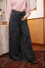 Jean de tiro alto con corte wide leg y pierna extra ancha, confeccionado en denim de lavado oscuro. Presenta bolsillos funcionales delanteros y traseros, con cierre frontal de cremallera y botón metálico.