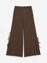 Pantalon blanco de corte amplio y tejido liviano con bordado floral en la parte inferior, aberturas laterales con tiras para atar y cintura elastizada.