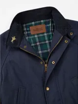 Campera tipo encerada de corte clásico para hombre, en color bordó, con cuello alto, cierre frontal con botones a presión metálicos y solapa, bolsillos frontales superiores ribeteados y bolsillos inferiores grandes con solapa y botón.