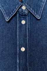 Camisa de denim azul oscuro con cuello solapa, manga larga con puños anchos y bajo asimétrico. Cierre frontal con botones blancos.