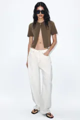 Chaqueta corta color verde oliva, de tejido de punto con cuello redondo y manga corta. Cierre frontal con un único botón dorado.