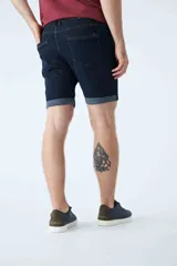 Bermuda de jean azul oscuro con diseño de cinco bolsillos, cierre de cremallera y botón, y detalle de botamanga doblada.