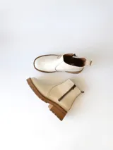Bota corta de cuero vacuno con textura granulada, color crudo. Presenta cierre lateral metálico, suela track de goma en tono suela y tirador trasero.